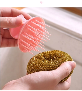 Detail of hand holding a pink kitchen handle brush and a gold wire scouring ball over a sink