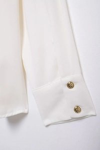 Close-up of white crepe blouse cuff featuring ornate gold buttons with embossed patterns