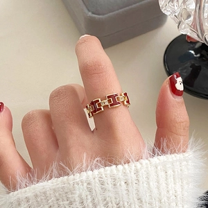 Close-up of gold plated ring with red enamel H-shape and zircon stones on hand