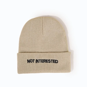 Close-up of khaki knit beanie featuring black 'NOT INTERESTED' letter embroidery on cuff