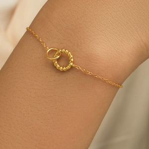 Detailed view of intertwined twisted and smooth gold rings on a delicate bracelet chain