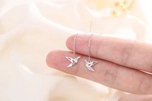 Macro view of silver paper crane earrings with tassels and sparkling zircon stones