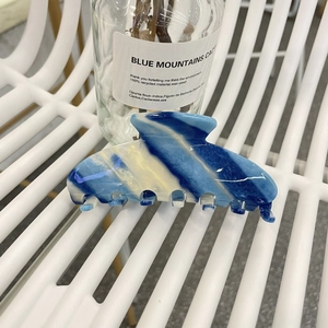 Blue and yellow marble pattern acetate hair claw clip shown on a minimalist chair