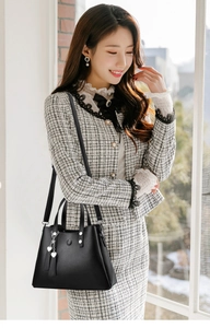 Chic sac à main noir avec breloque cœur présenté avec un élégant tailleur à carreaux