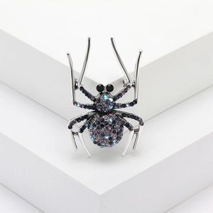 Spider brooch pin with purple and blue rhinestones on a minimalist white platform