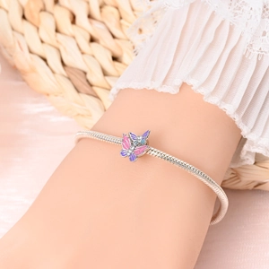 Détail de breloques papillon en émail rose et violet sur un bracelet en chaîne serpent argent