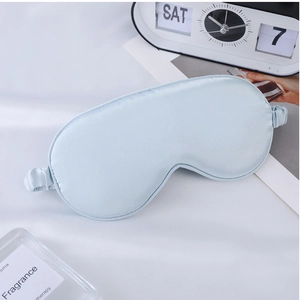 Light blue faux silk sleep mask displayed with an alarm clock and fragrance items