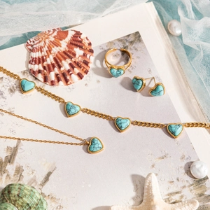 Parure bijoux cœur turquoise avec collier doré et bague sur un fond de thème plage
