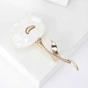 Macro shot of white pearlescent flower brooch with gold accents and metallic leaf detail