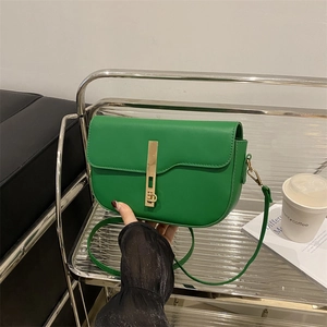 Green minimalist saddle bag for women with a vertical gold metal lock and shoulder strap