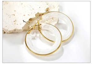 Close-up of golden stainless steel hoop earrings with cream resin inlay on a stone base