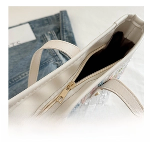 Detail of smooth metal zipper closure and textured floral fabric on beige tote bag