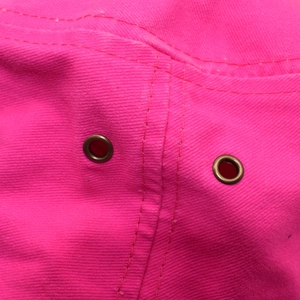 Detail of breathable bronze eyelets and reinforced stitching on pink washed cotton fabric