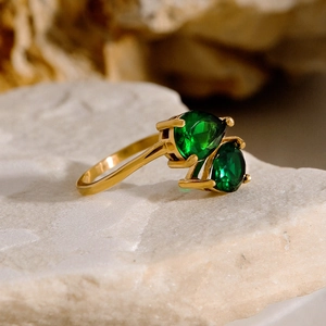 Detail of gold open ring featuring two pear-cut green stones on a white natural stone base