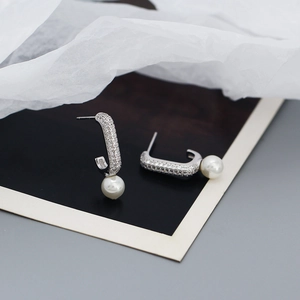 Detailed view of silver J-shaped earrings with zircon pavé and hanging white pearls