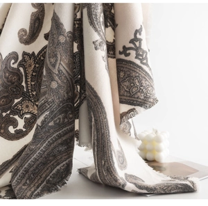 Detailed close-up of paisley pattern wool blend scarf with fringe tassels in warm tones