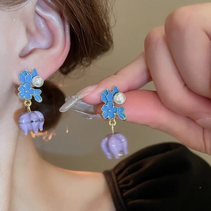 Close-up of gold-plated flower earrings with blue petals, pearls and purple lily pendants