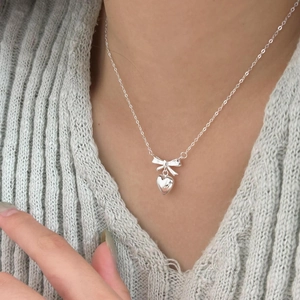 Minimalist 925 sterling silver necklace featuring a bow and heart pendant on a model