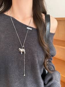Close-up of a silver pony pendant on a long chain worn over a grey knit sweater