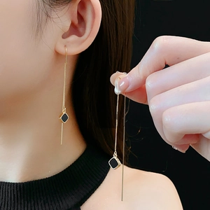 Dettaglio di lunghi orecchini a catenella dorati con pendente quadrato nero su modella