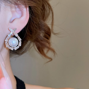 Close-up of pearl drop earrings with geometric zircon frame worn by a model