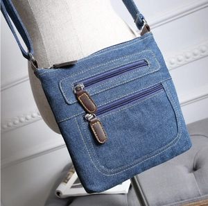 Blue denim crossbody bag featuring multiple zippers and adjustable strap on a model