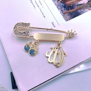 Detail of a gold pin brooch featuring Hamsa, Allah script, and crown charms on a magazine