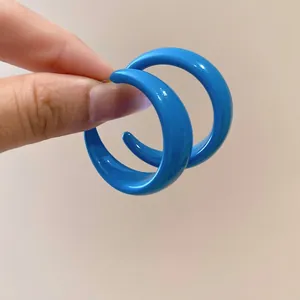 Vibrant blue acrylic C-shaped hoop earrings with a glossy finish shown in hand