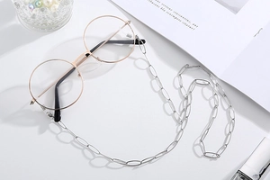 Silver thick large oval link eyeglass chain shown with round frame glasses on white surface
