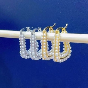 Detailed close-up of square pearl hoop earrings in gold and silver finish on a bar