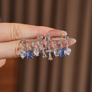 Detail view of silver safety pin earrings with blue zircon heart and cross pendants