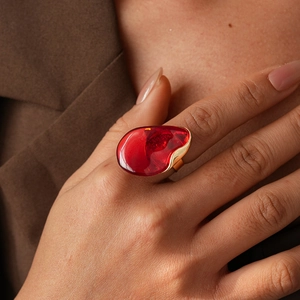 Détail d'une bague dorée artistique avec une grande pierre en résine rouge de forme goutte