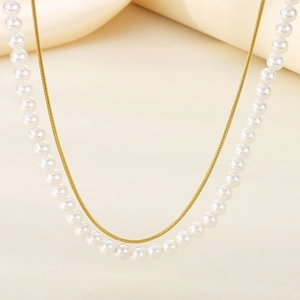 Elegant double-layer necklace featuring white pearls and golden snake chain on beige fabric