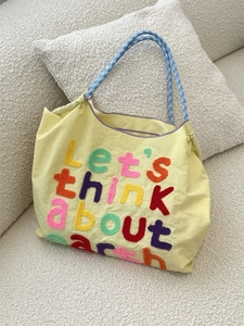 Detail of yellow canvas tote bag with towel embroidery and blue plaid handles