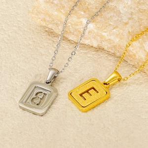 Close-up of gold and silver initial pendants B and E on natural stone background