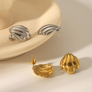 Artistic close-up of shell-shaped 18k gold and silver studs in a ceramic tray