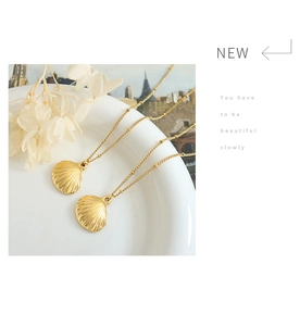 Detailed view of two gold scallop shell pendant necklaces on a white ceramic plate