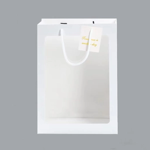 Close-up of white gift paper bag with transparent window, rope handles and small tag