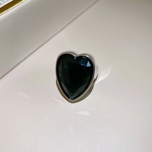 Detailed view of a silver heart ring with a large faceted emerald green gemstone