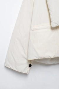 Detailaufnahme einer weißen Steppjacke mit schwarzem Knopf am Ärmel und Taschendetails