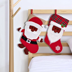 Paio di calze natalizie con Babbo Natale nero appese a una spalliera del letto in legno.