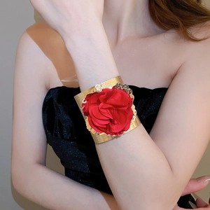 Detail of a wide gold metal cuff bracelet with a large red fabric flower and wavy edges