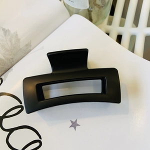 Close-up of a matte black square hair claw clip on a minimalist white aesthetic background