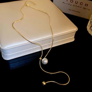 Detail of a gold snake chain necklace with a white pearl charm on a jewelry box