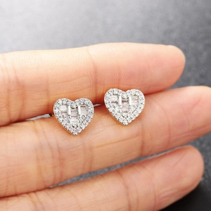 Hand holding silver heart stud earrings with cubic zirconia and golden base