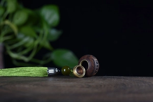 Macro shot of sandalwood hollow pendant with brass cap and light green silk tassel