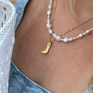 Detail of layered gold cowboy boot pendant necklace and white baroque pearls on model