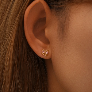Detail of s925 silver gold bow earrings with pink heart-shaped crystal on female ear