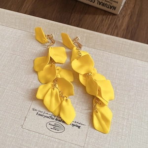 Detailed view of yellow matte flower petal tassel earrings on a textured cream backdrop