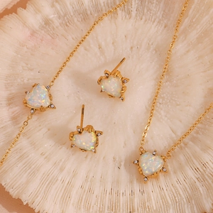 Macro view of a gold-plated heart-shaped white opal jewelry set on a white coral base